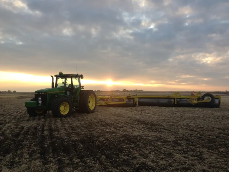 Tractor and field equipment beneath a low sun and a cloud-filled sky