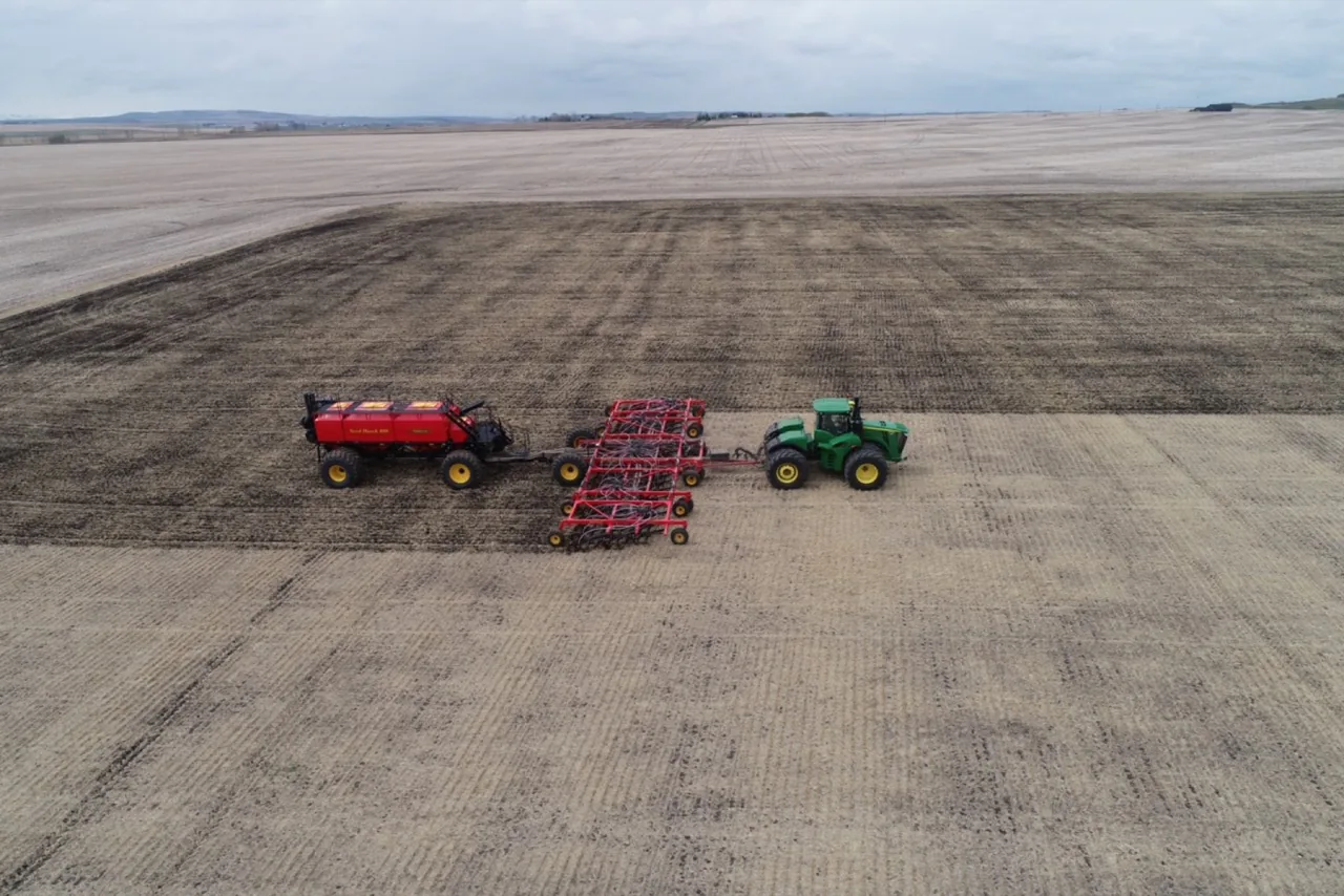 A tractor and seeding equipment making a wide pass across a field, seen from above
